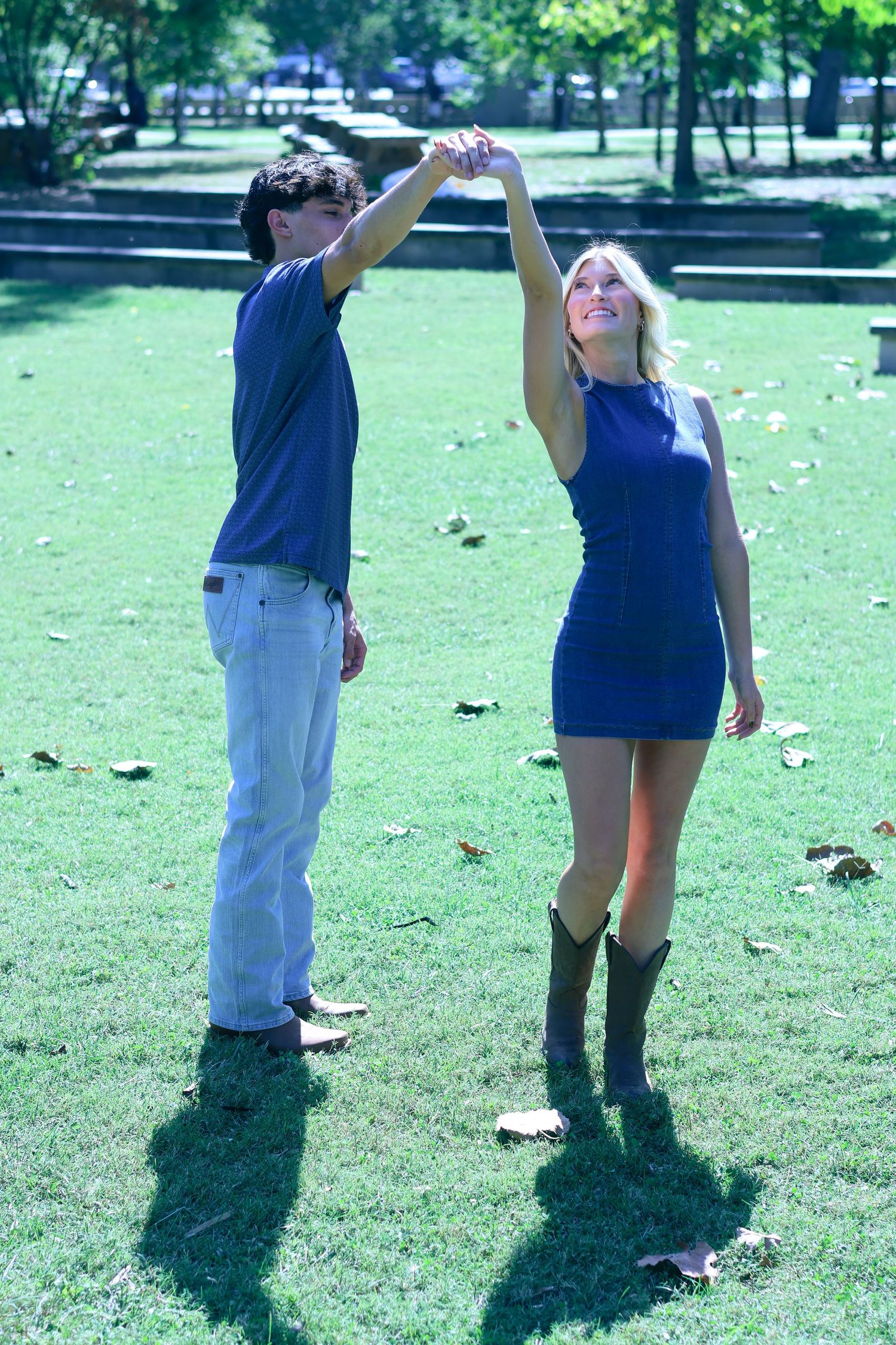A couple in coordinating outfits dances together on green grass in a park.