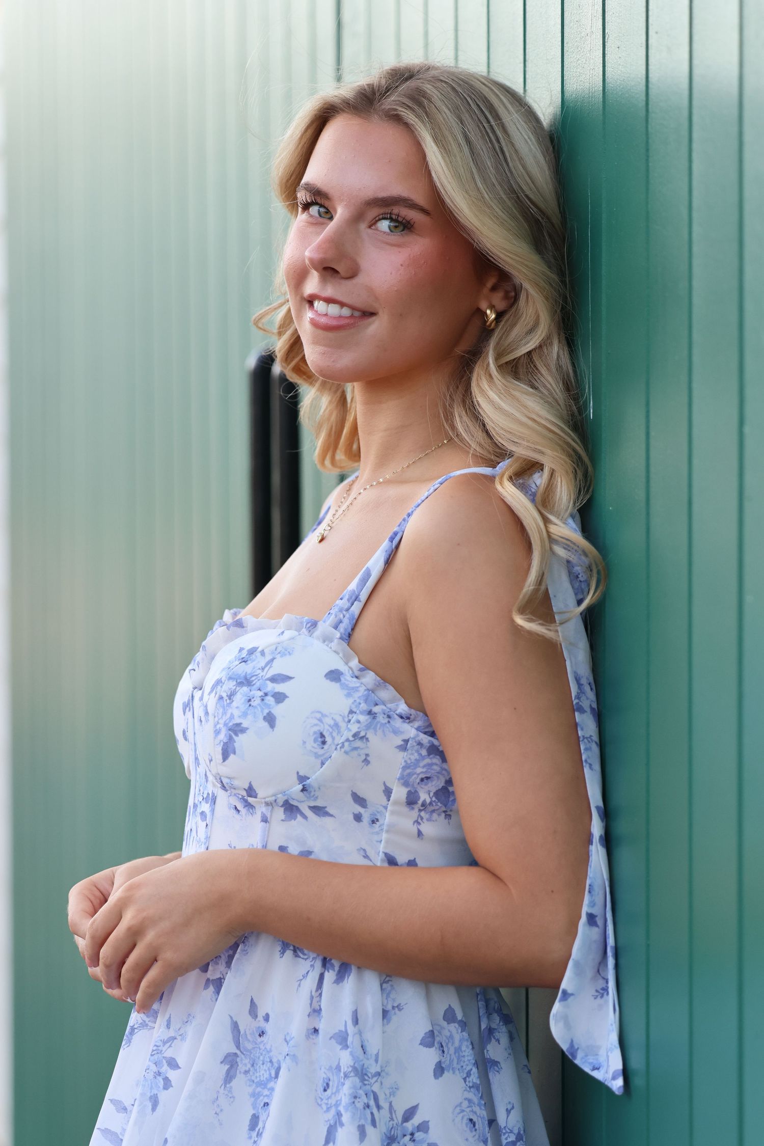 Woman in a light blue floral sundress poses against a turquoise wall in three different positions.