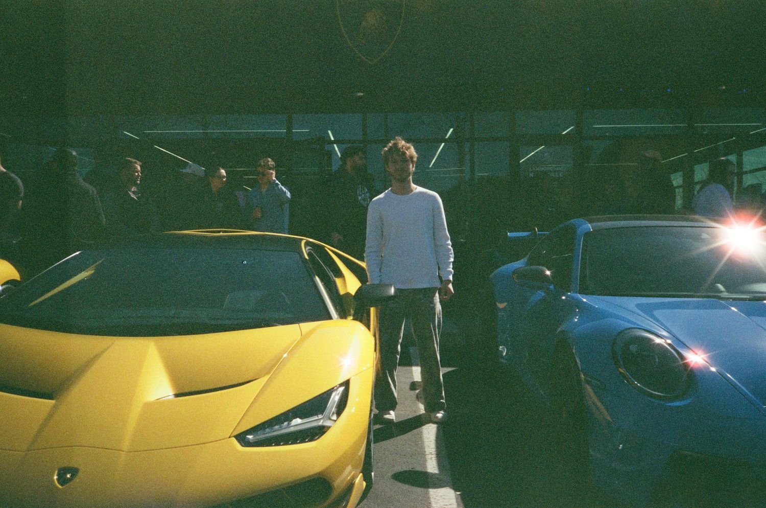 35mm photograph of a young man between 2 luxury cars.