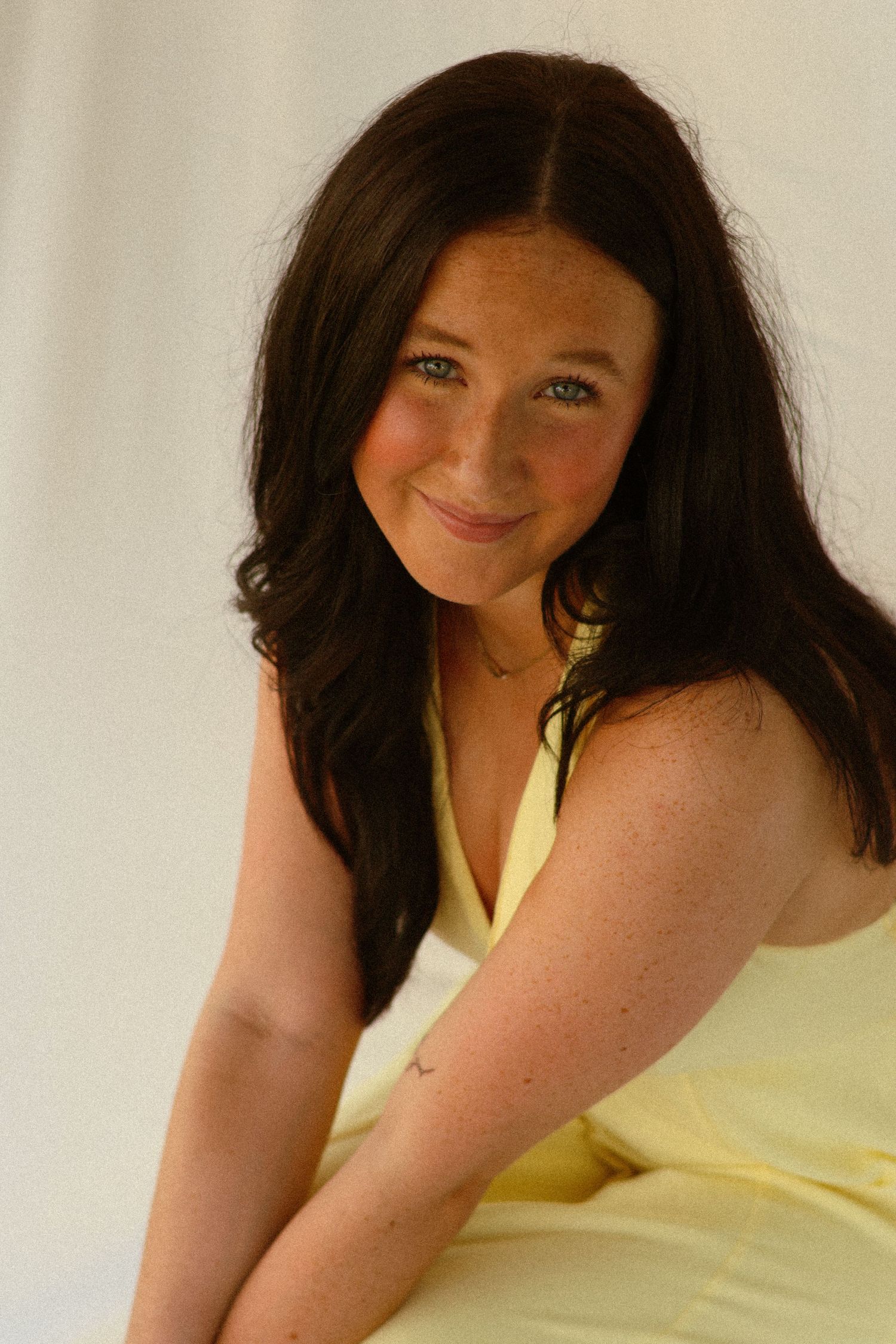 Young woman with dark hair and blue eyes in yellow halter dress smiling warmly.