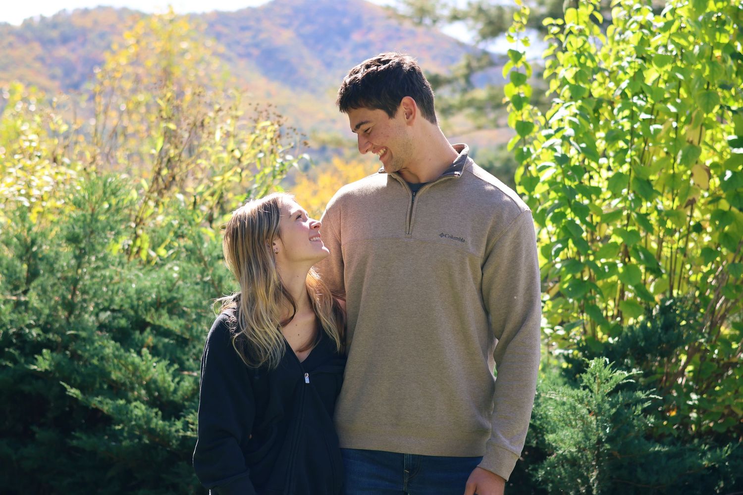 Couple shares intimate moment in outdoor setting with mountains and greenery.