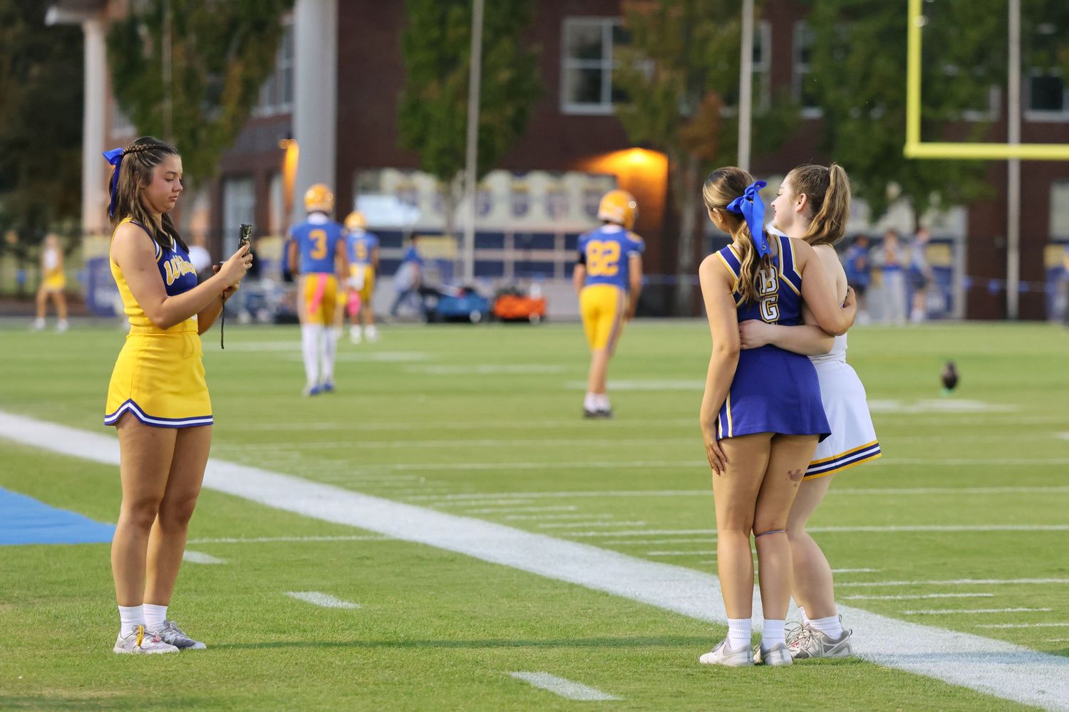 Cheerleaders perform on the sidelines of a football field during a sunny day.