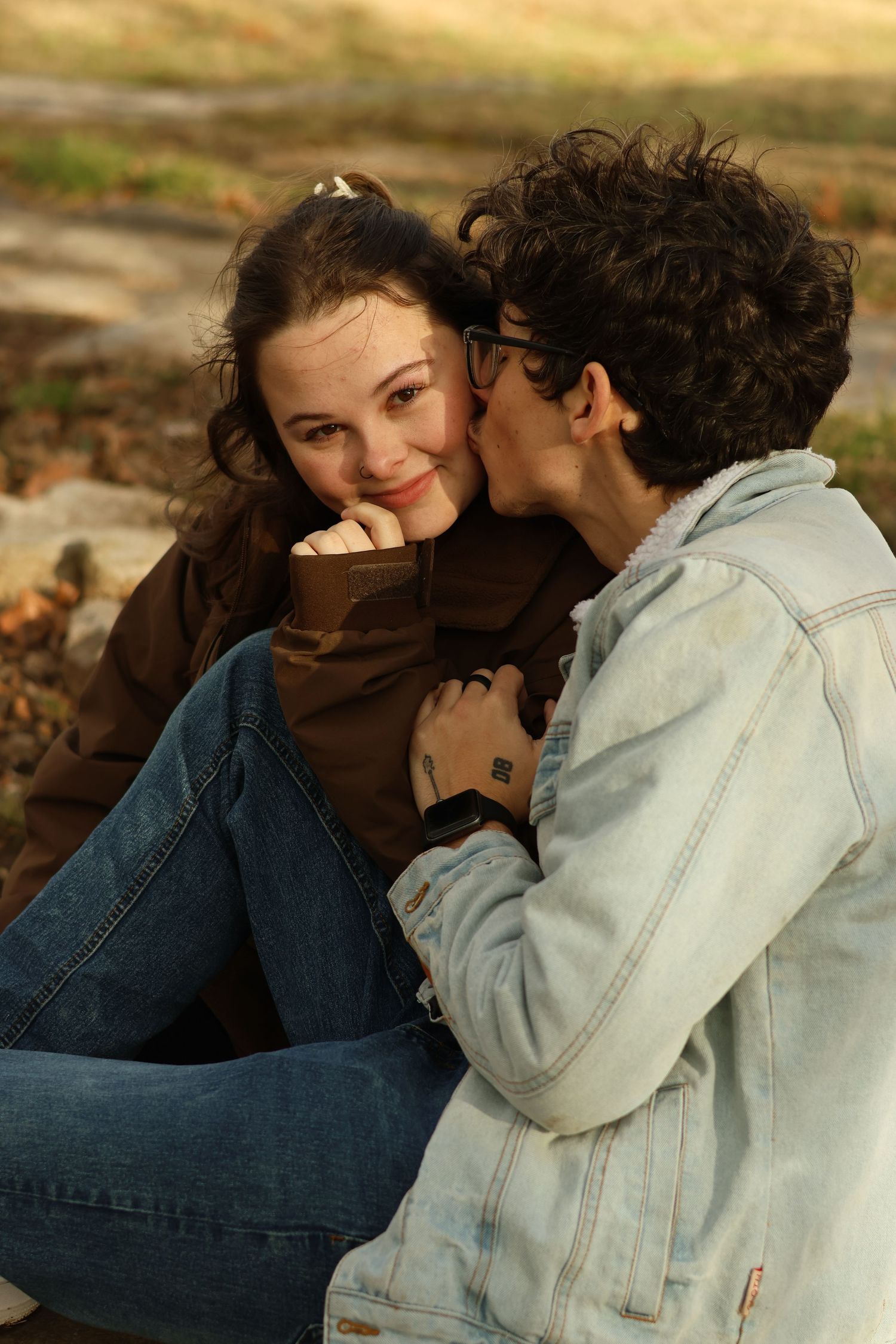 A couple shares tender romantic moments while sitting together outdoors in casual denim and light colored clothing.