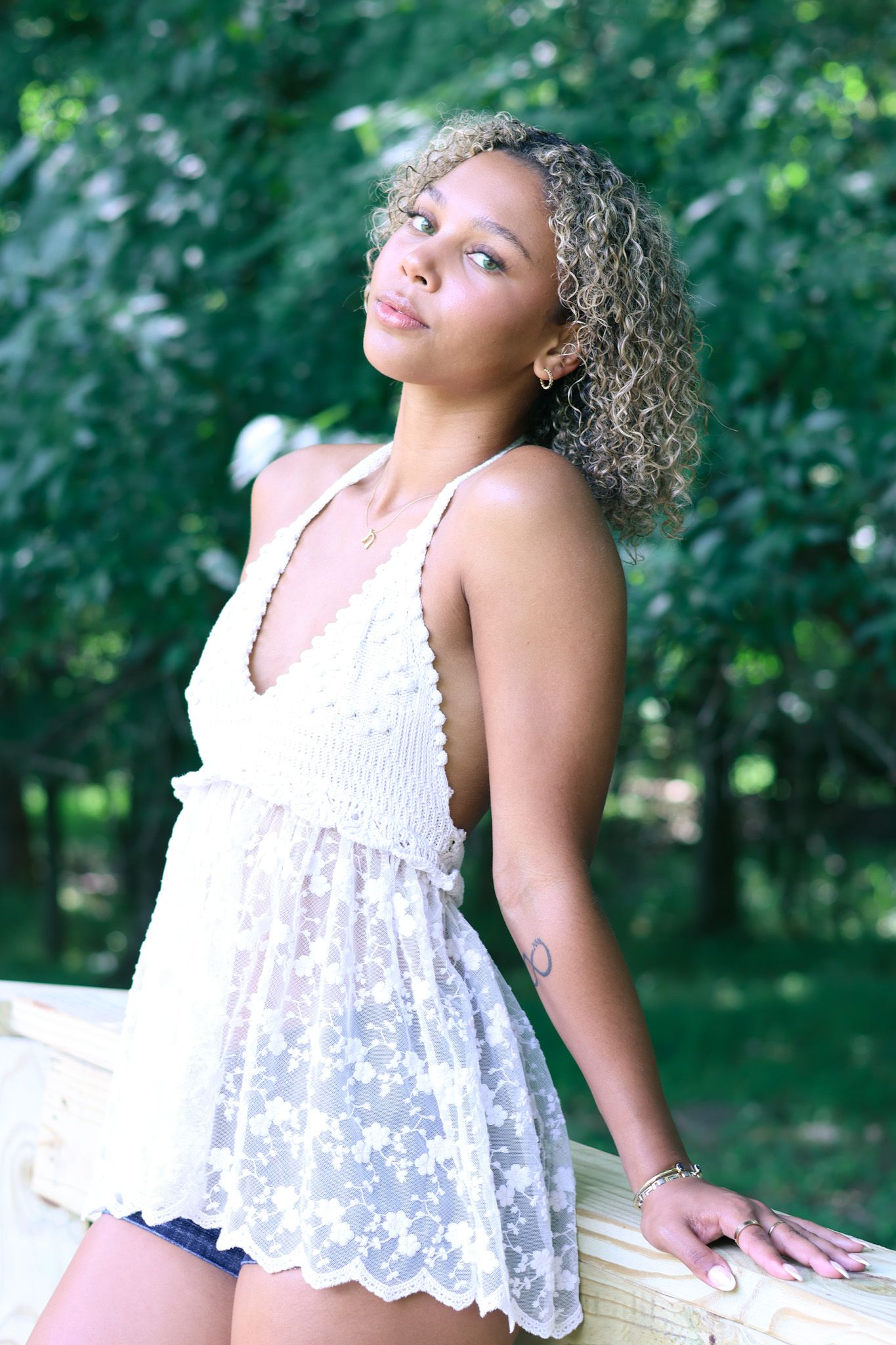Person in white lace top poses against natural forest background.