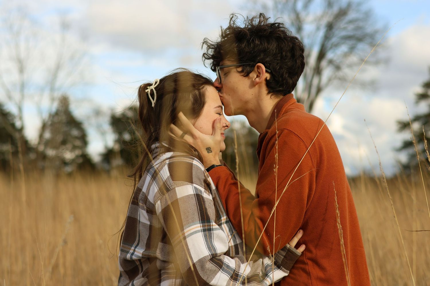 Romantic couple sharing a tender kiss in a golden autumn field at sunset.