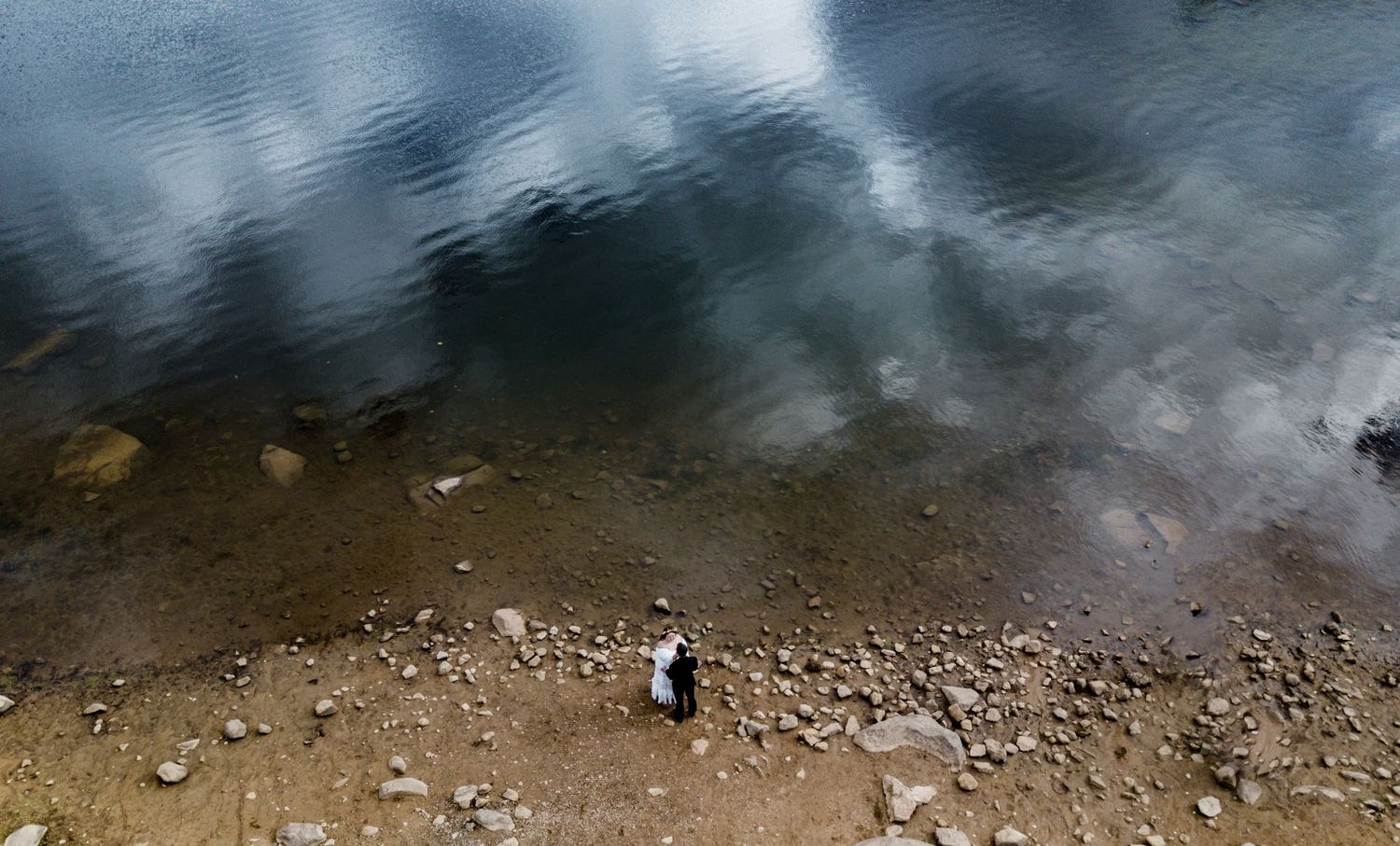 Aerial view of a person standing on rocky terrain near cloudy water.