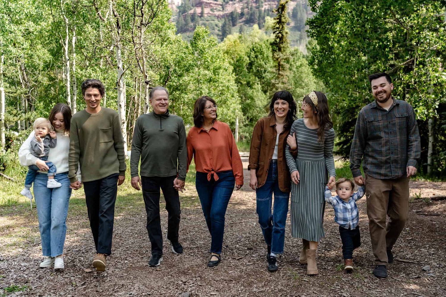 Group walking together on forest trail with mountains and aspen trees in background.