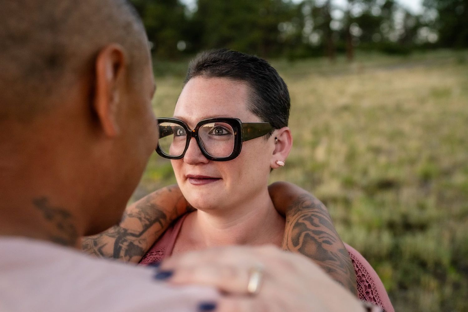 A couple shares an intimate moment in a field with mountains visible in the background.