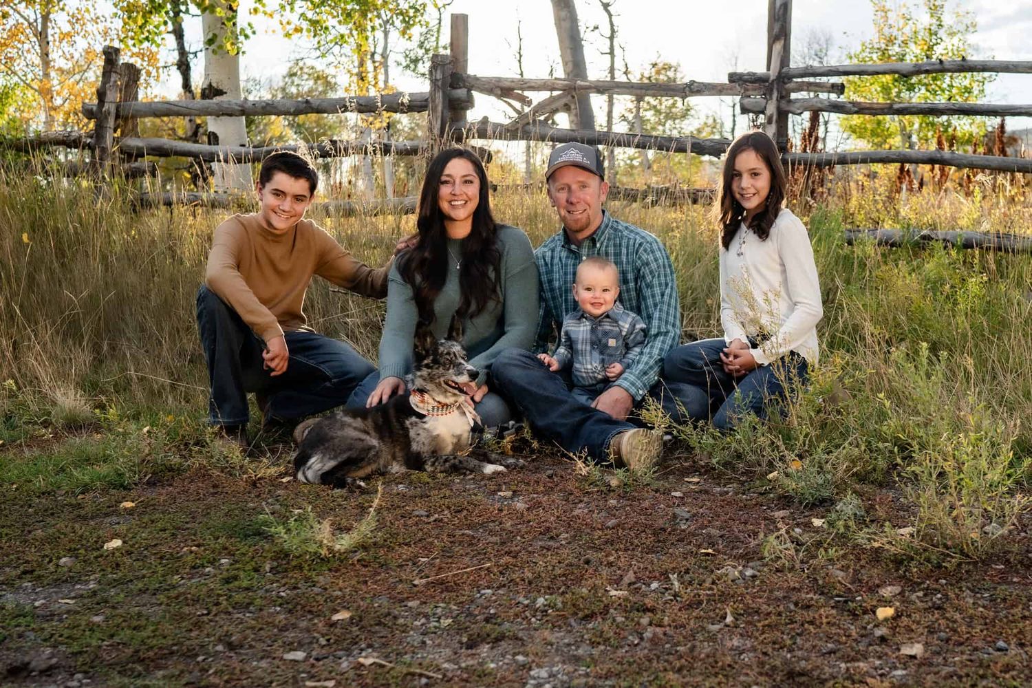 Family group sitting together with their dog by a rustic wooden fence at sunset.