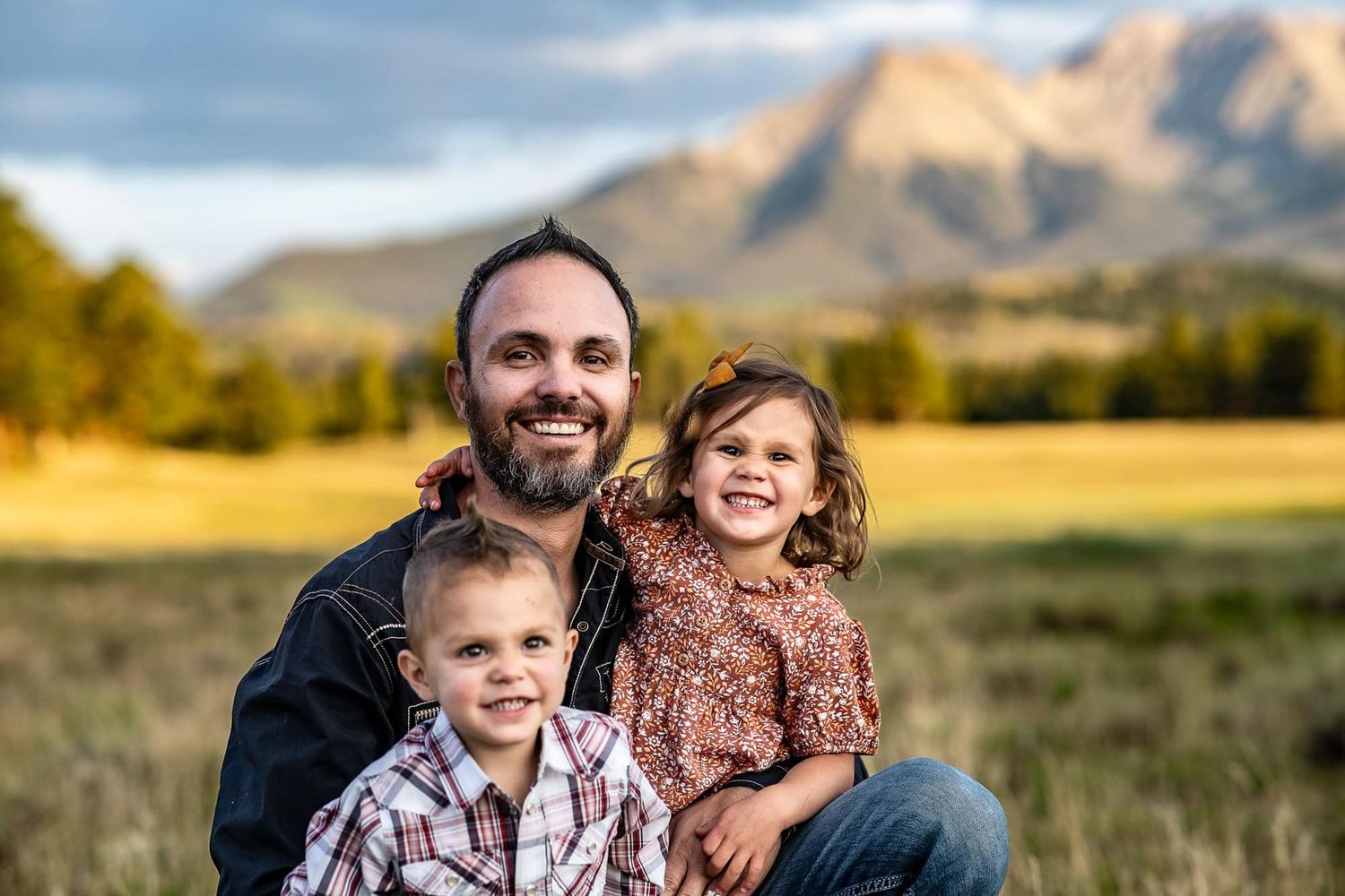 Happy family portrait with mountain landscape in background during golden hour.