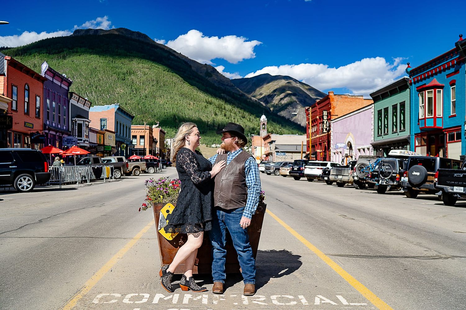 Group stands in middle of colorful historic mountain town street with vibrant storefronts and mountain backdrop.