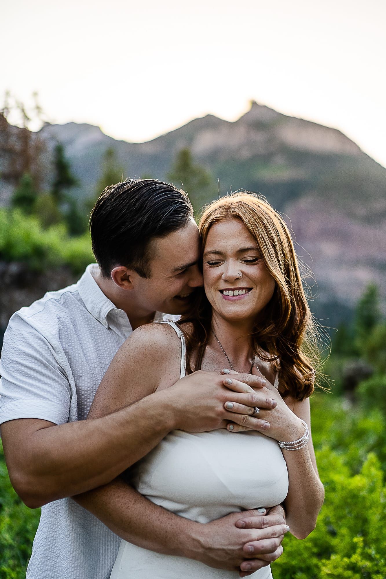 Intimate portrait of couple embracing and smiling against mountain backdrop.