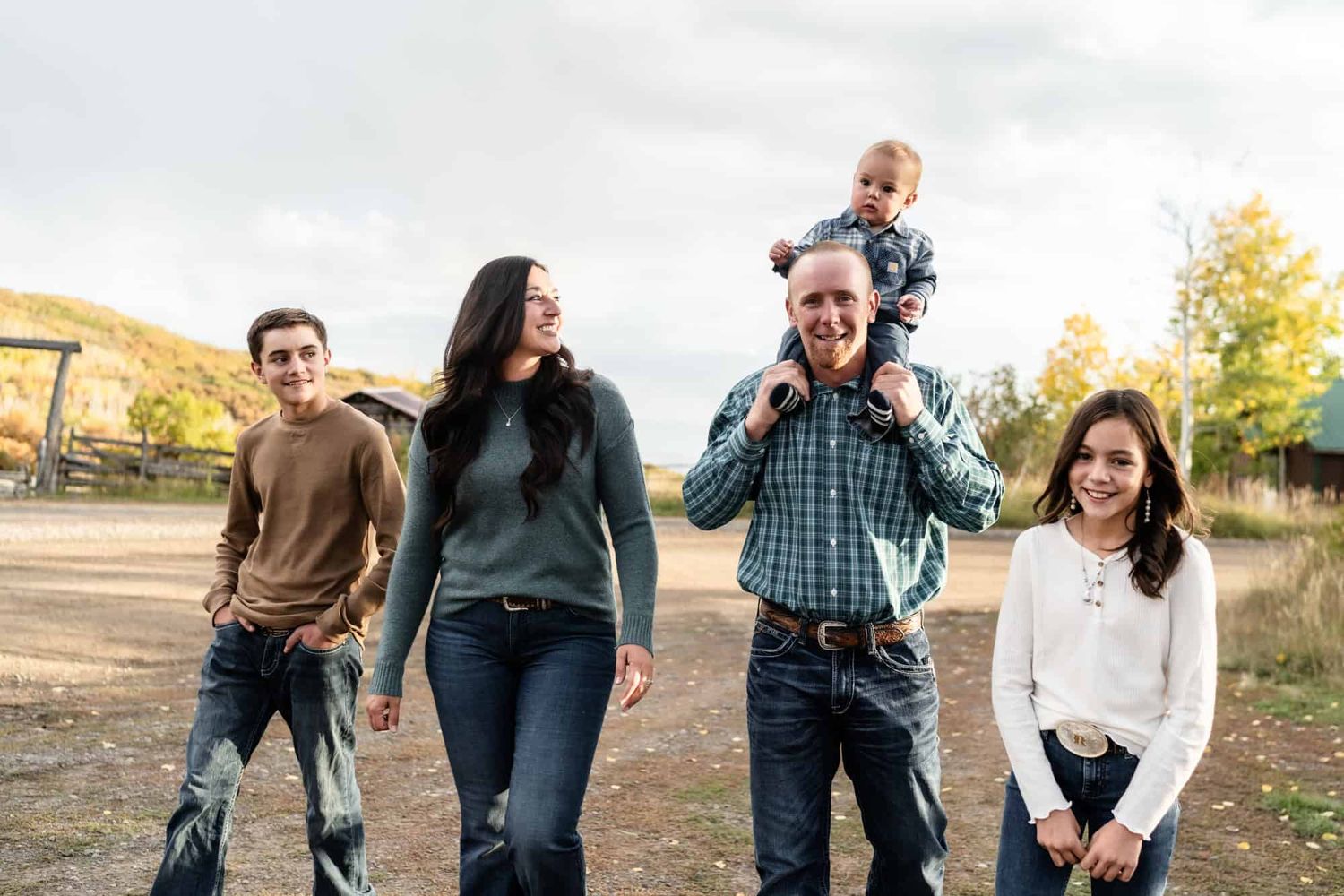 Family of four walking together outdoors with one child riding on shoulders.