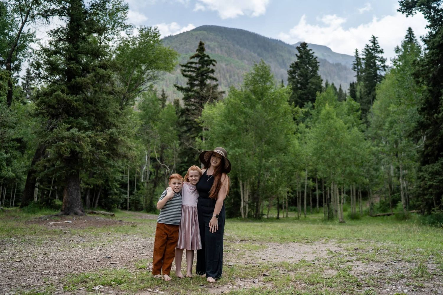 Family group standing together against mountain backdrop with evergreen trees.