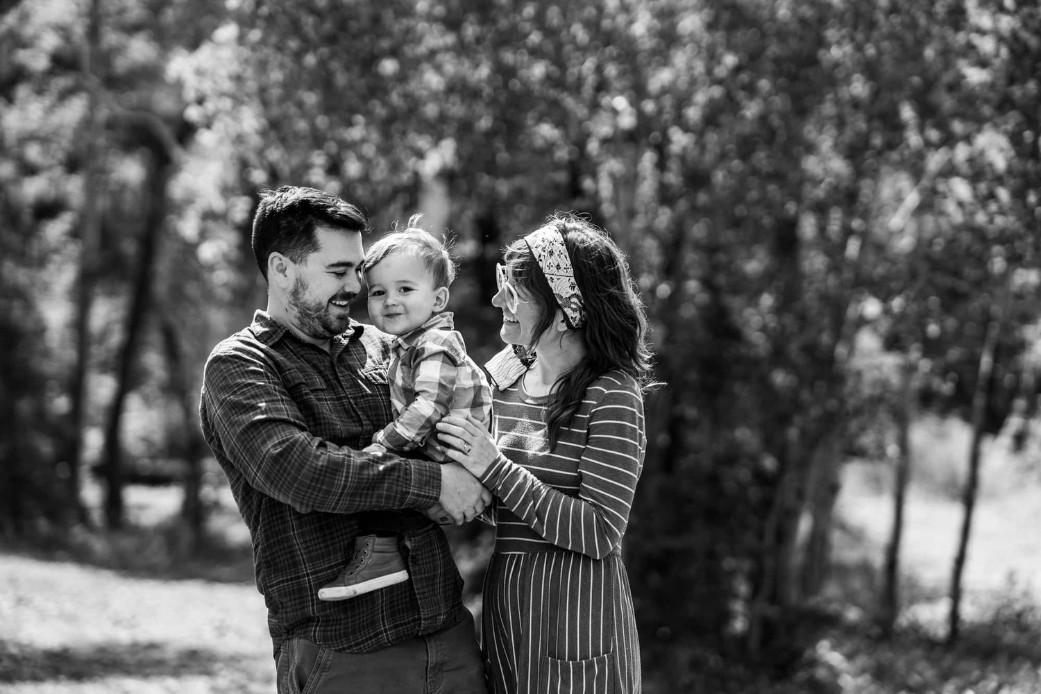 Black and white portrait of family sharing joyful moment outdoors among trees.