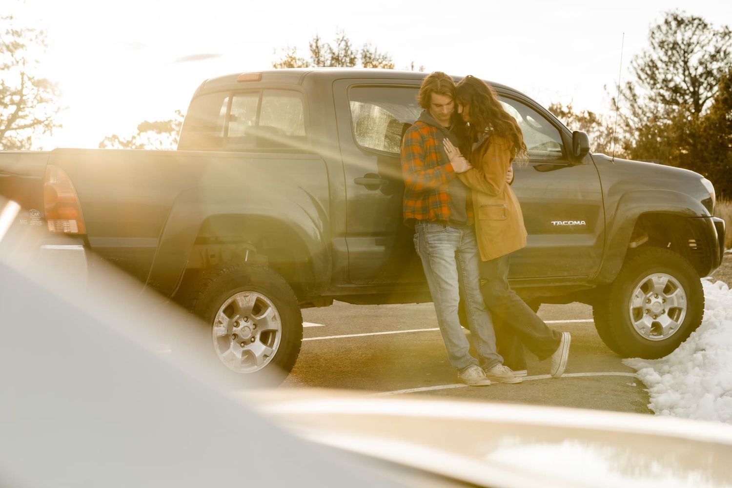 A couple stands by their pickup truck during golden hour sunset.
