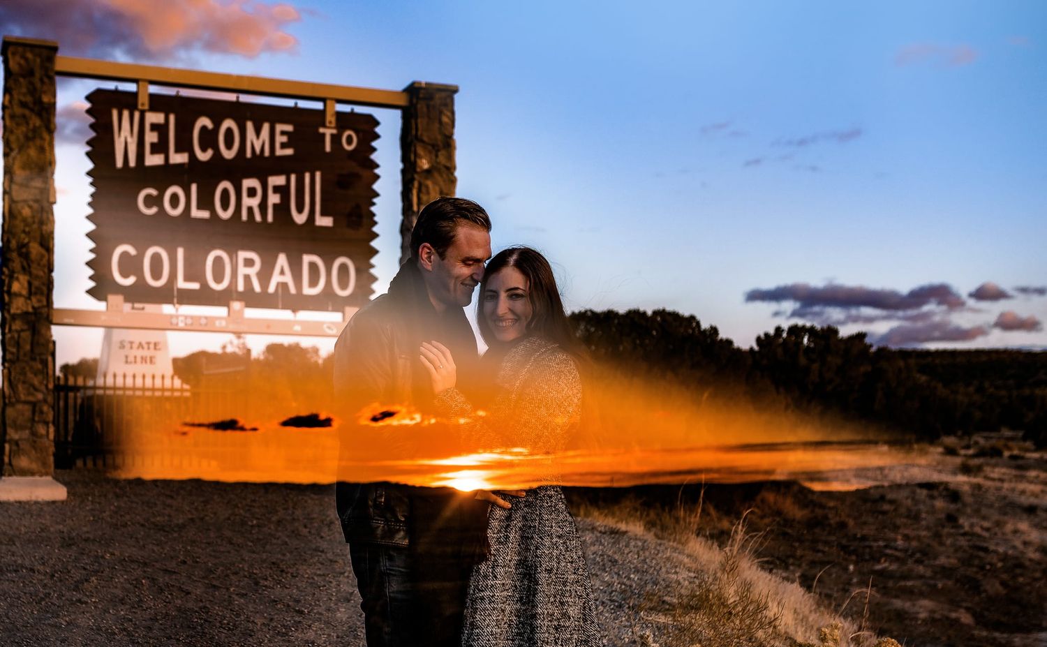 A couple embraces by the Colorado welcome sign during a golden sunset.
