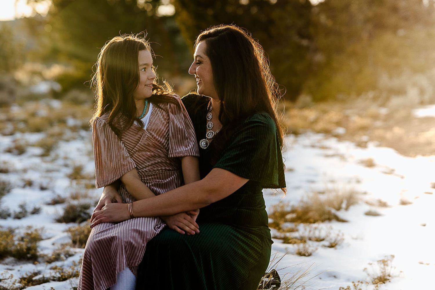 Two people share an intimate moment while sitting together in a snowy outdoor setting at sunset.