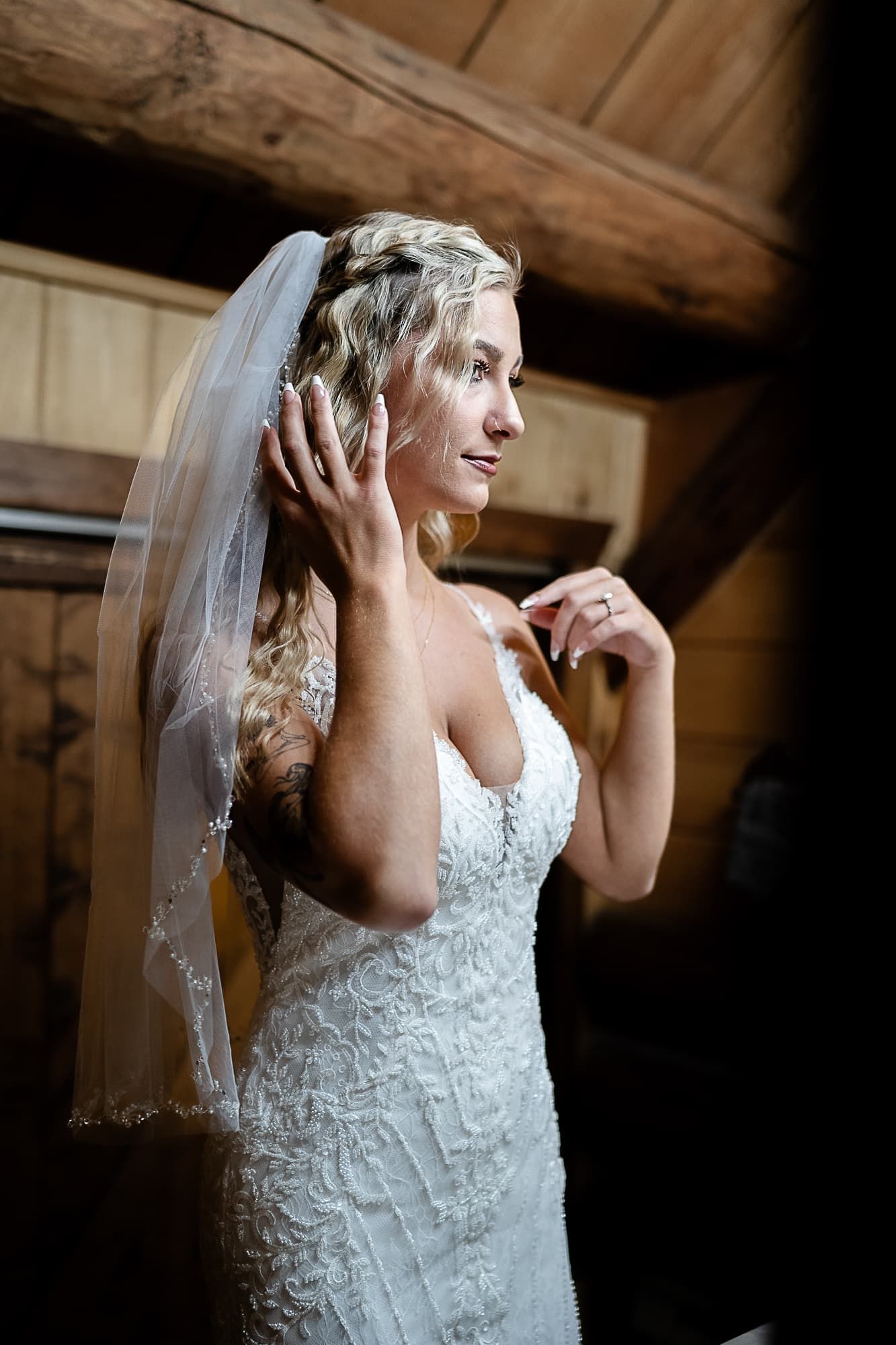 Elegant lace wedding dress with flowing veil captured in rustic wooden cabin setting.