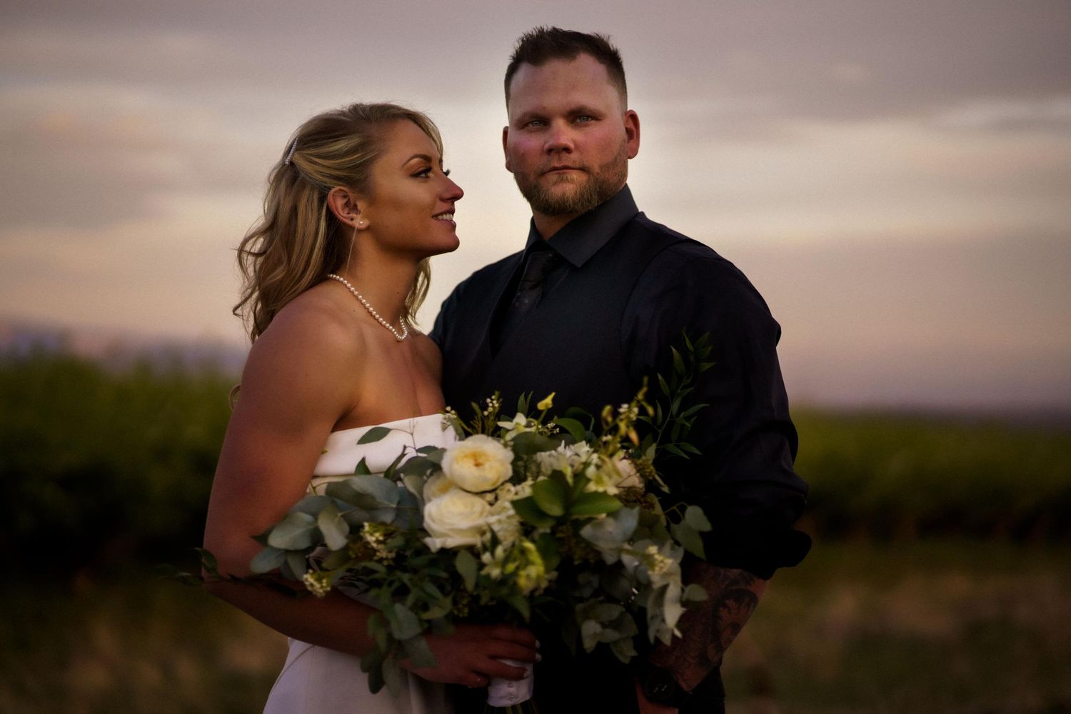A romantic outdoor wedding portrait at sunset with a white bouquet featuring elegant greenery and white flowers.