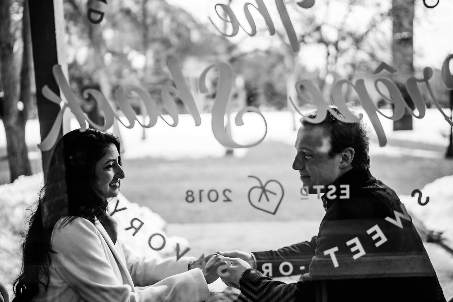 A black and white photo of a couple holding hands with decorative window reflections.