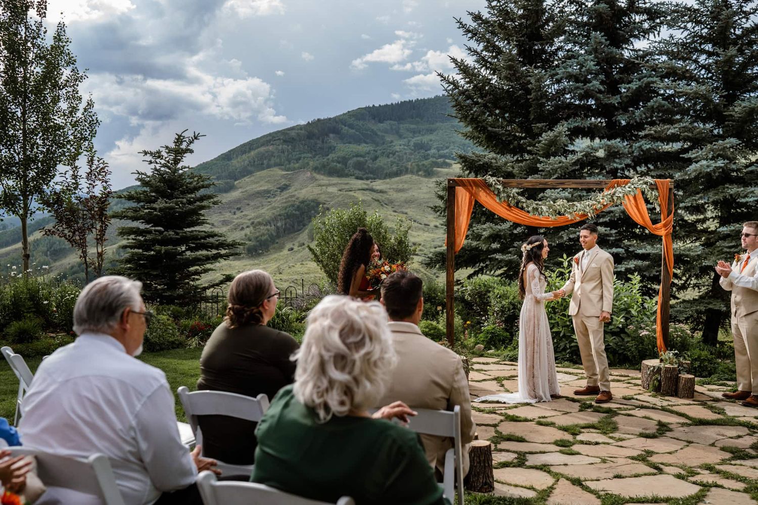 Mountain wedding ceremony under wooden arch with evergreen trees and mountain vista in background.