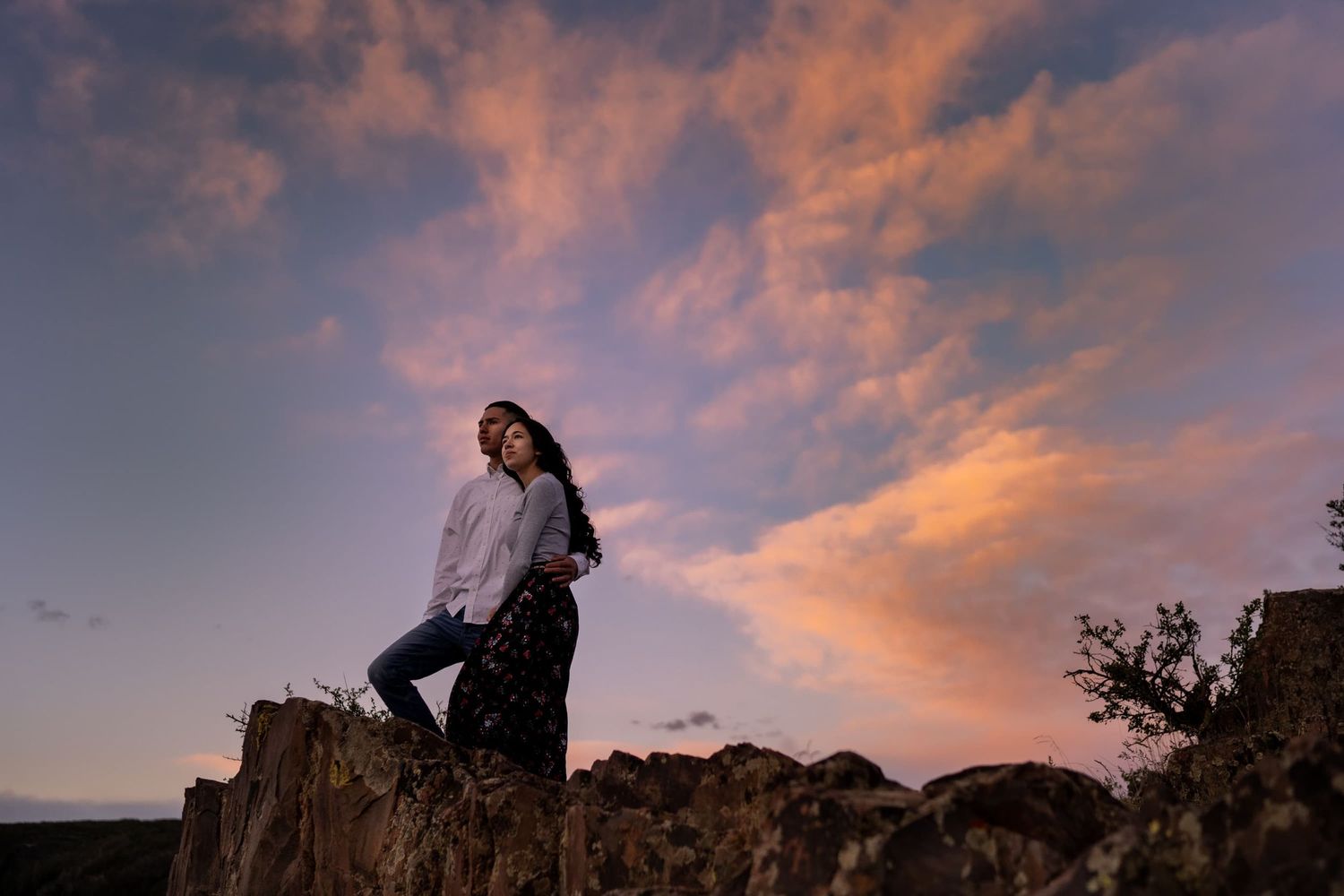 Silhouette figure stands on rocky outcrop against dramatic purple and orange sunset sky.