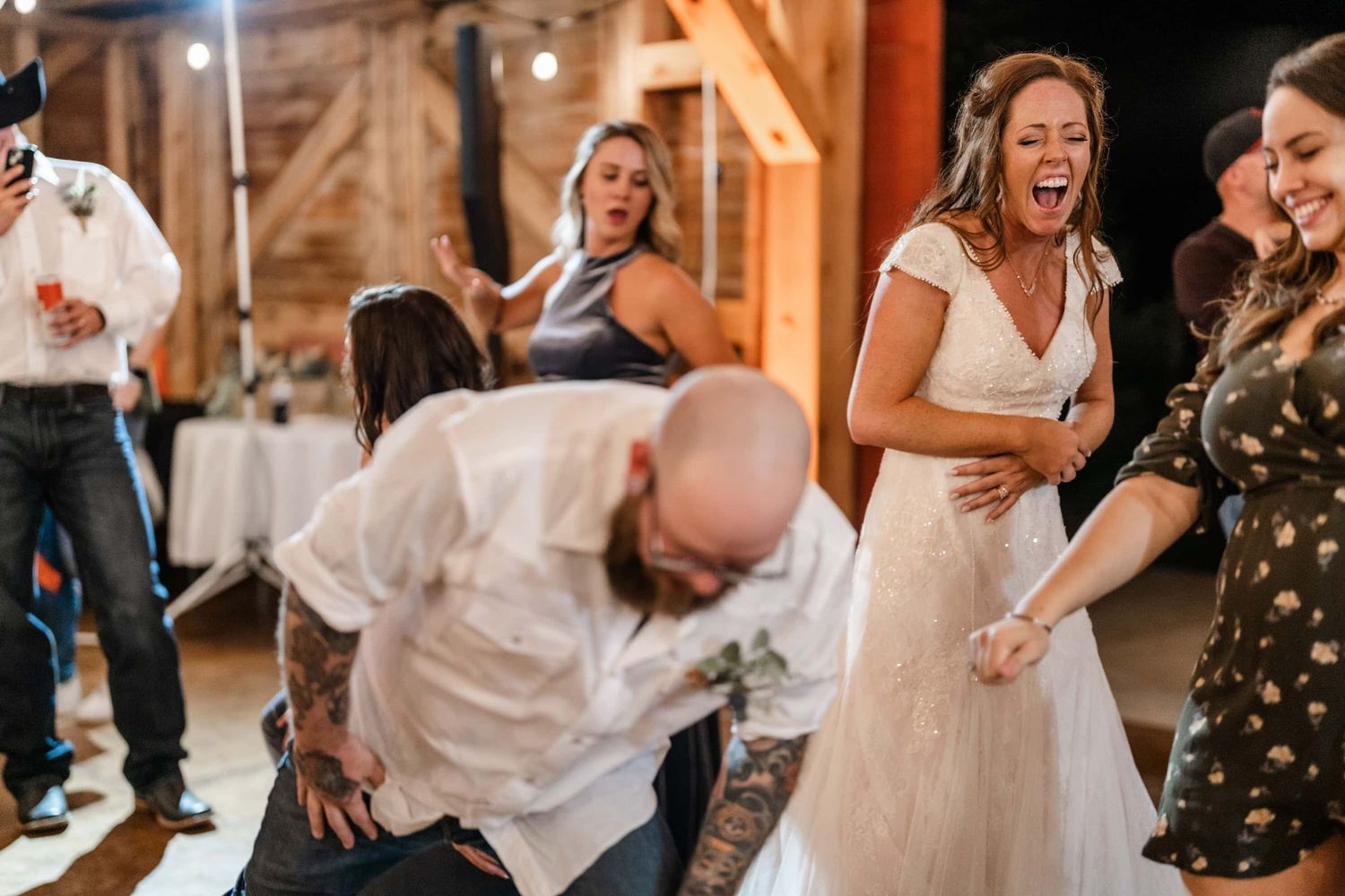 Wedding guests dancing enthusiastically on wooden dance floor at barn reception.