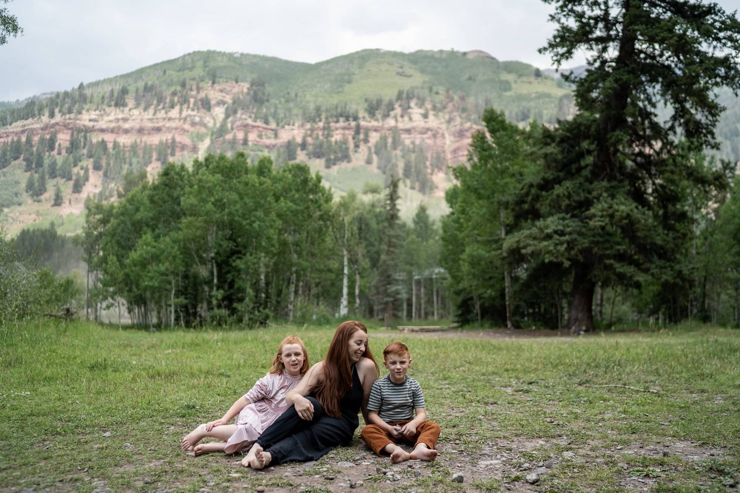 Group relaxing on grassy hillside with mountain vista in background.