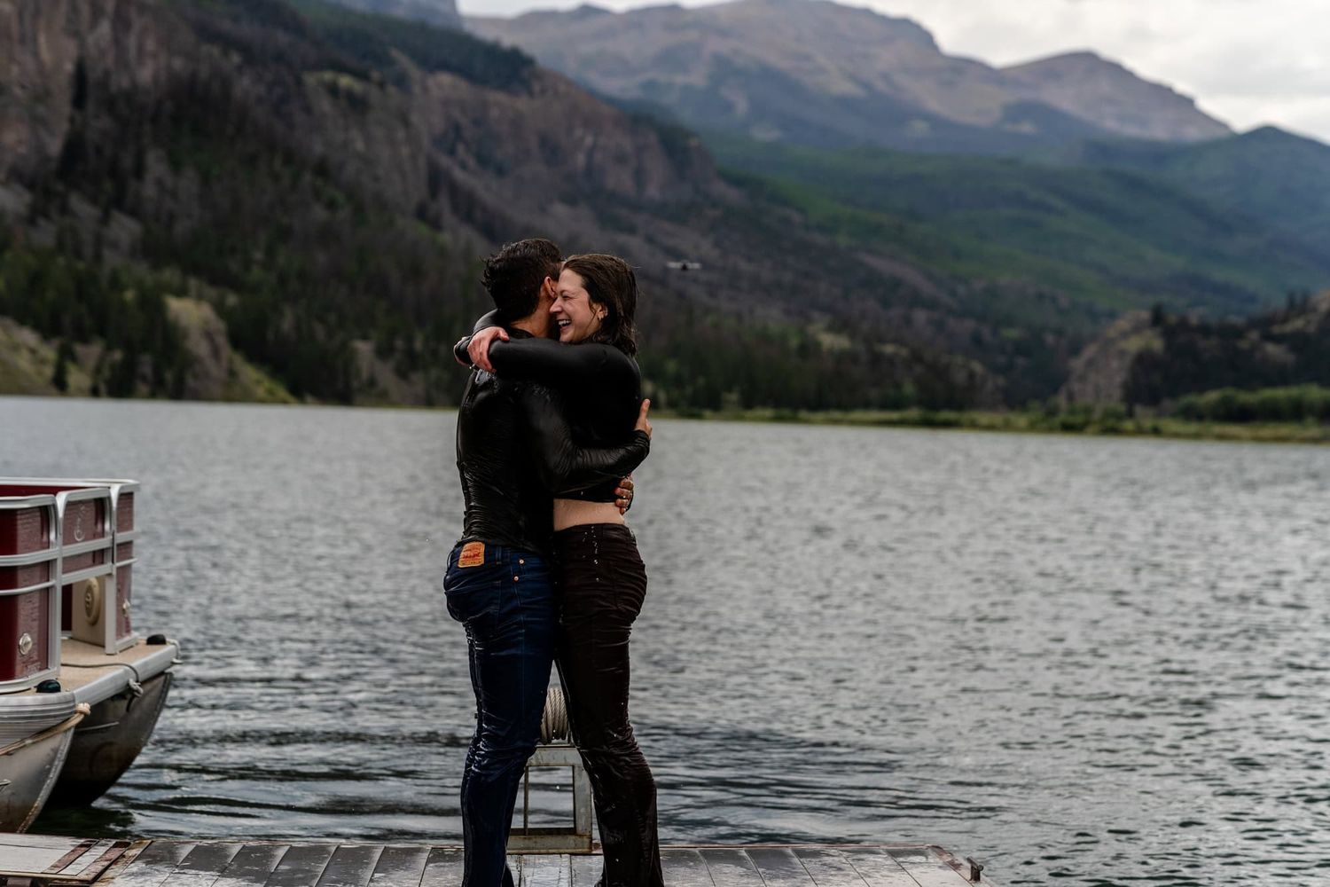 A romantic embrace on a lakeside dock with majestic mountains in the background.