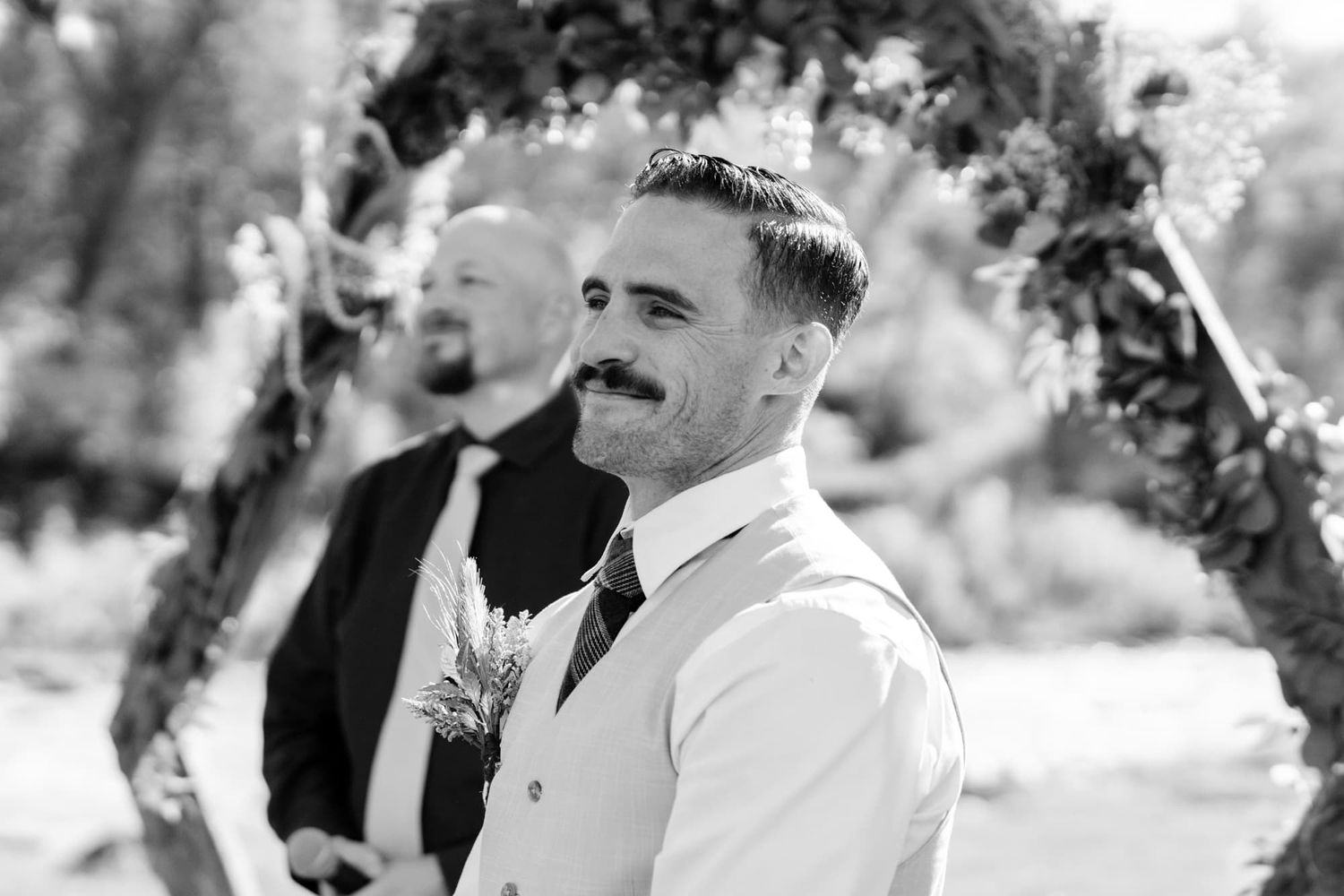 Black and white portrait of joyful reactions during wedding ceremony under floral arch.