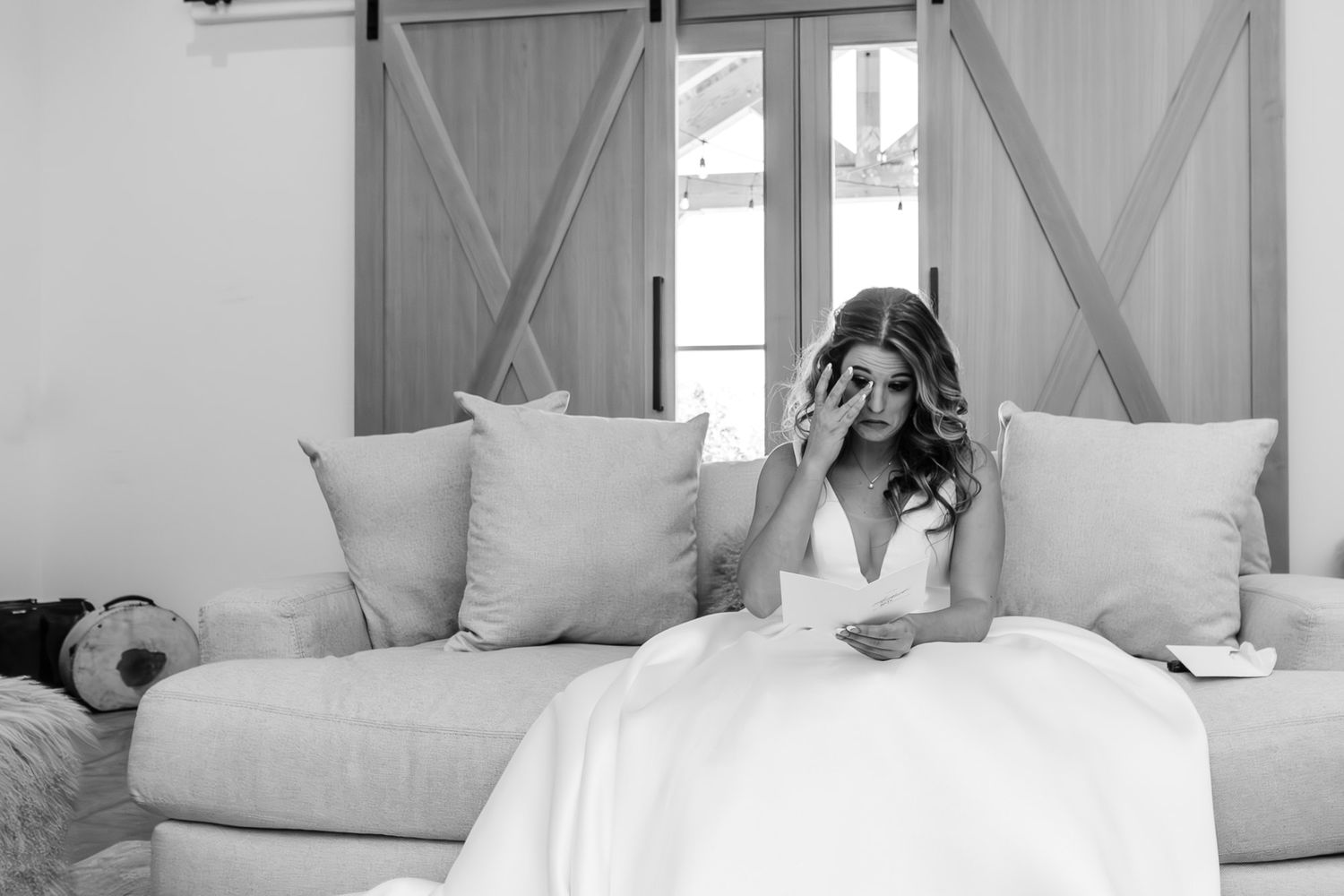 Candid moment of preparation in white wedding dress on gray couch. Image was taken elegant barn venue near Montrose Colorado.