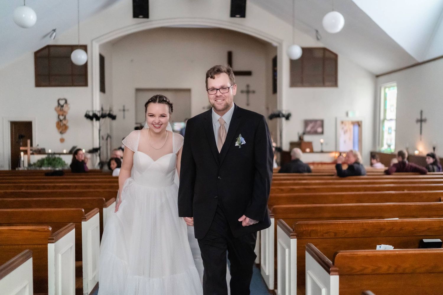 Wedding couple walking down church aisle between wooden pews.