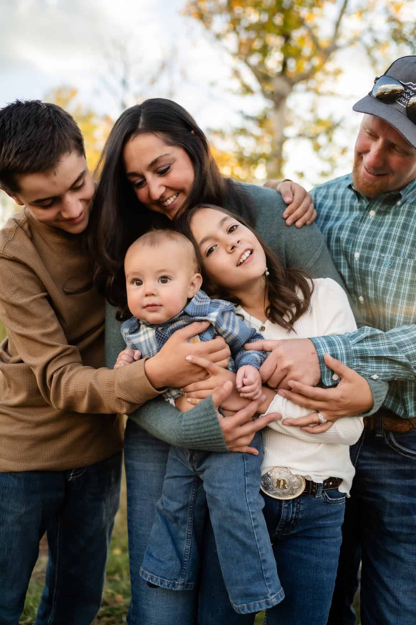 Multi-generational family sharing a playful moment together outdoors with autumn trees in background.