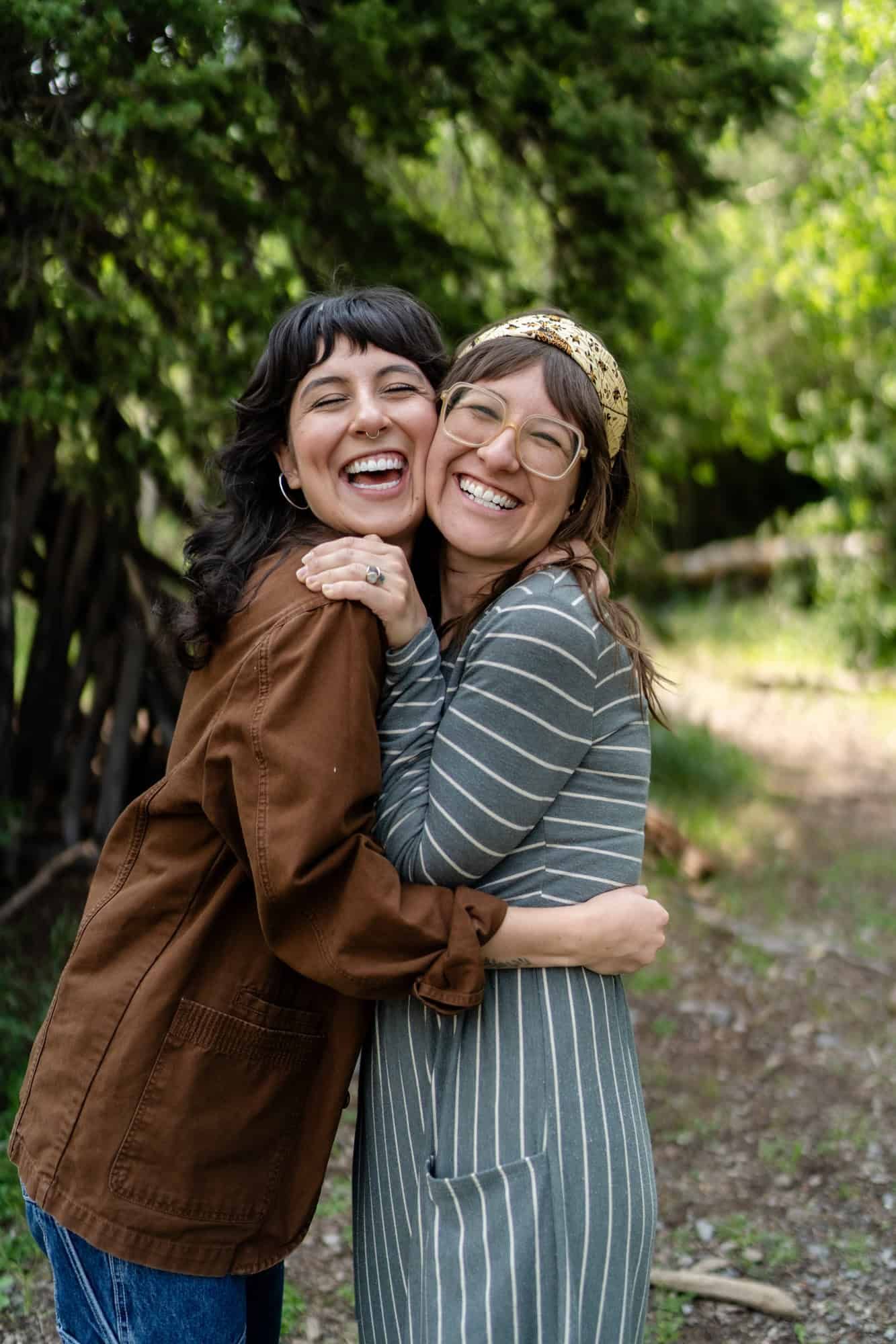 Two people sharing a joyful embrace and laughter on a forest path.