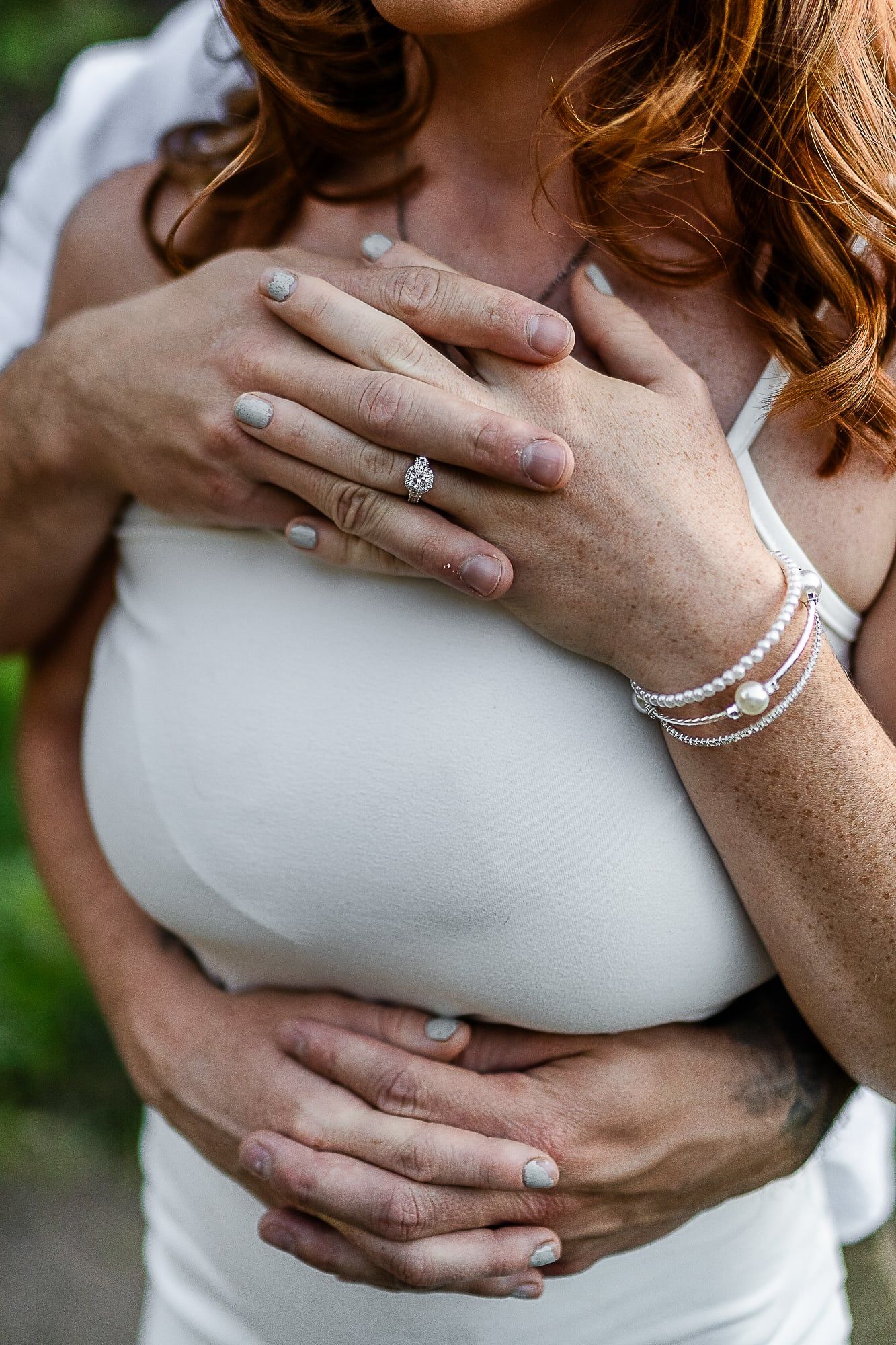 Close-up of hands wearing elegant jewelry and bracelet against a white dress.