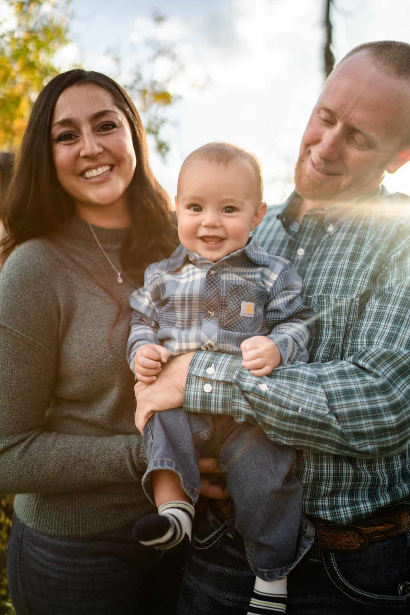 Happy family moment outdoors with baby wearing plaid shirt during golden hour.
