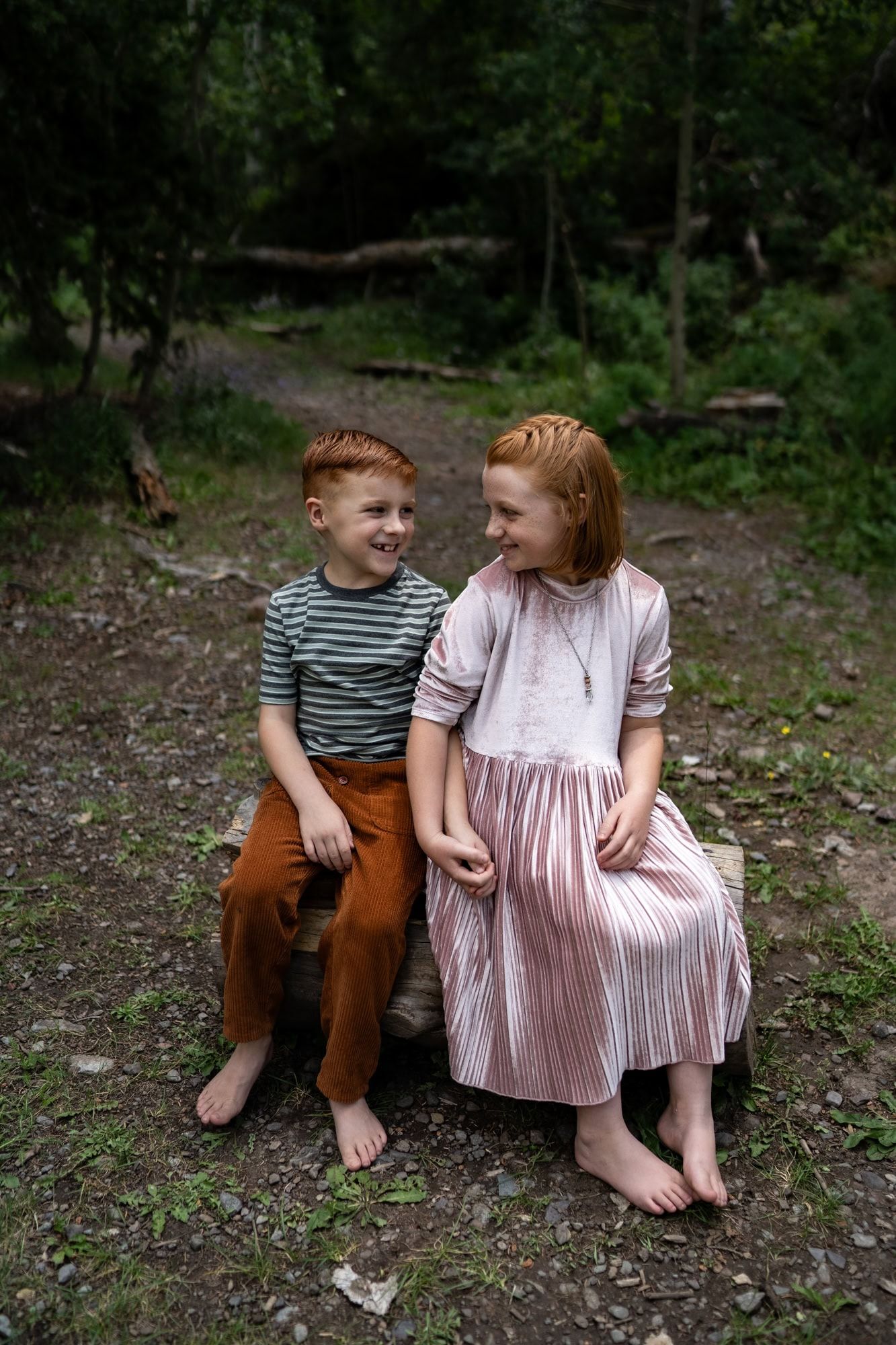 Two people sitting on fallen log in forest sharing a happy moment.