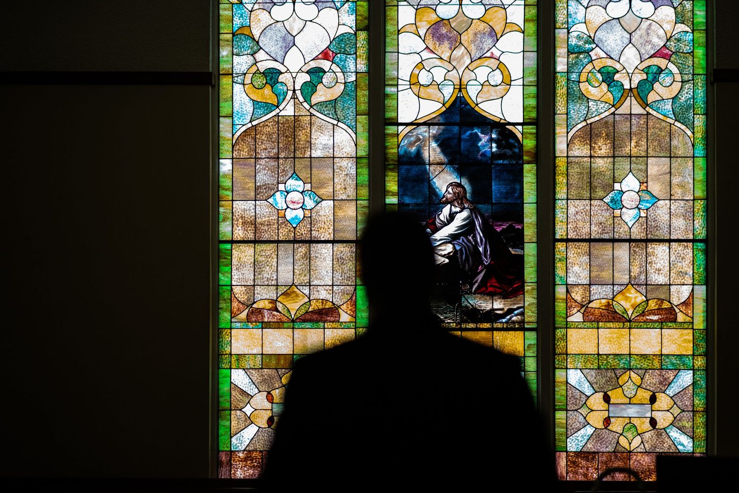 Silhouette against colorful stained glass church windows with ornate floral patterns.