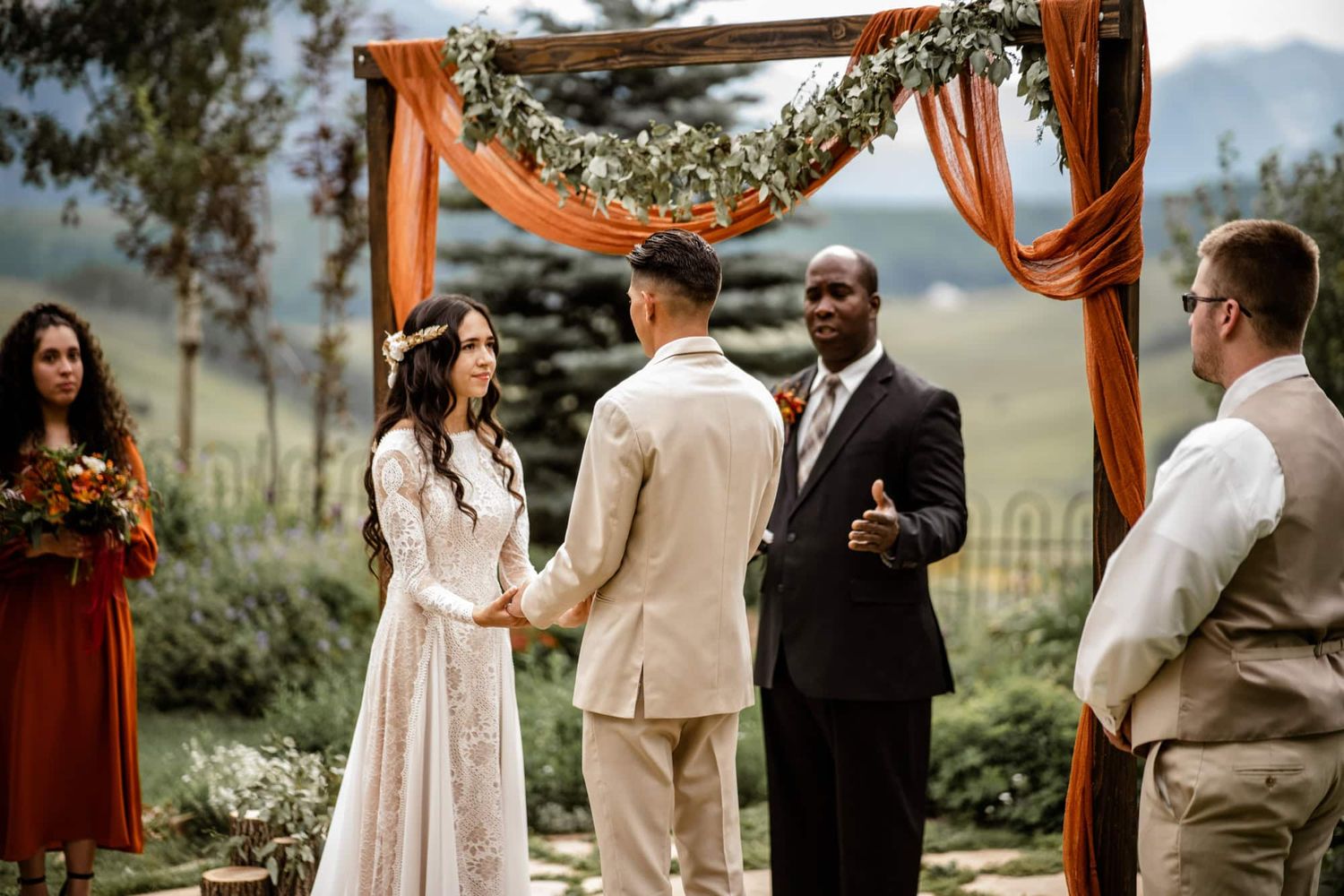 An outdoor wedding ceremony under a draped arch with mountain views and autumn-colored decor.