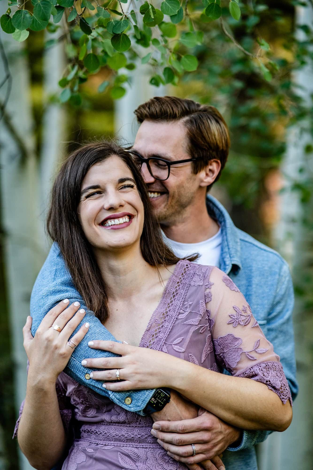 A happy couple sharing a candid laughing moment under green foliage.