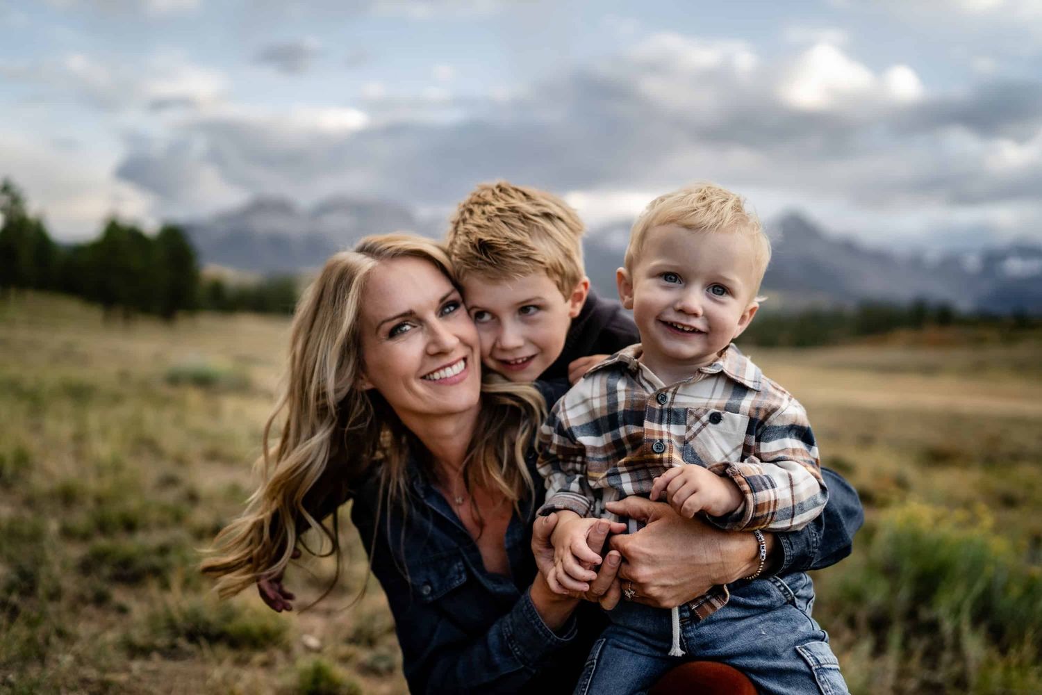 A touching family portrait against a mountainous backdrop with two young children in plaid shirts.