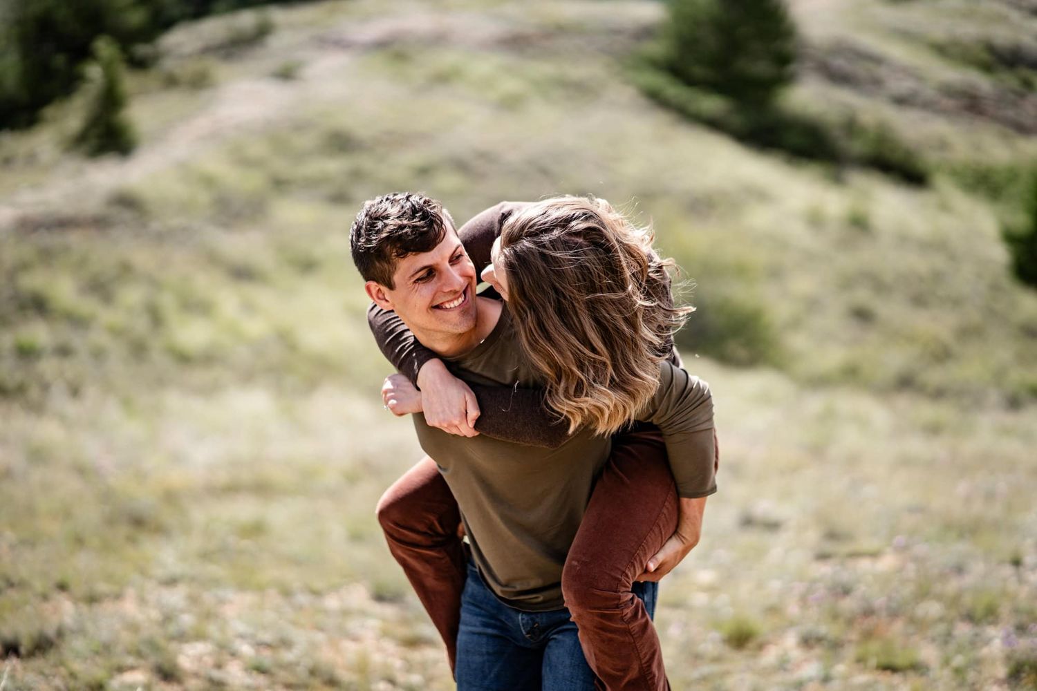 Joyful piggyback ride moment on a grassy hillside with mountains in the distance.