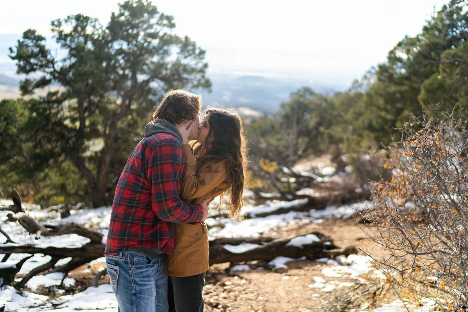 A couple shares an intimate moment while enjoying a snowy mountain vista on a hiking trail.