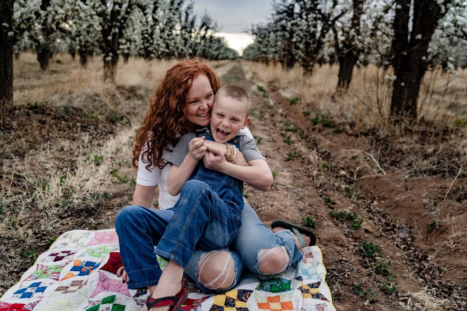 A tender moment between parent and child sitting on a colorful blanket outdoors.