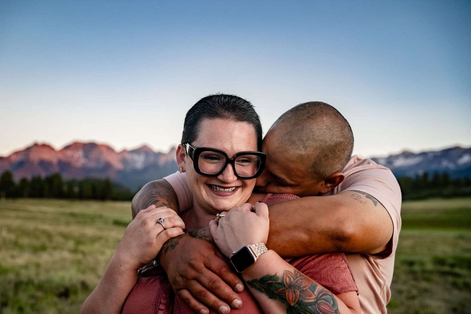 Couple embraces lovingly in a mountain meadow at sunset. A photographer from Montrose Colorado captured this at Top of the Pines in Ridgway.