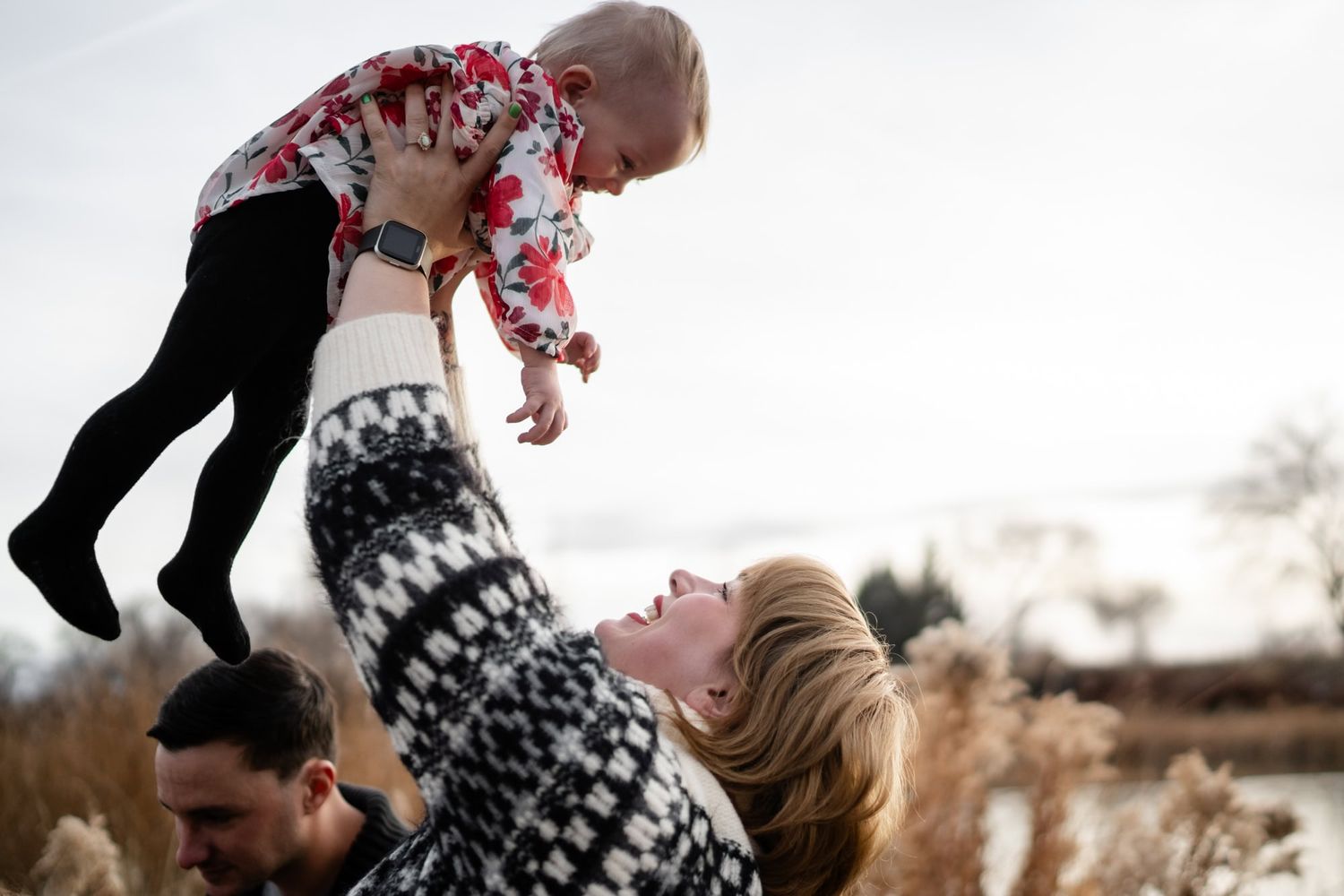 Parents playfully lift their child in the air during an outdoor photoshoot.