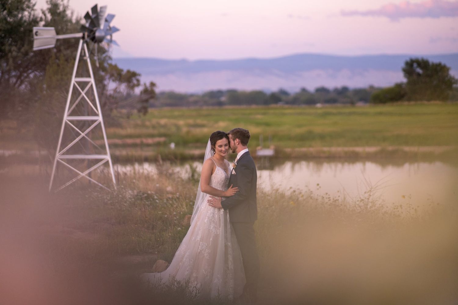 Romantic couple embracing in a field at sunset with a windmill tower in the background.
