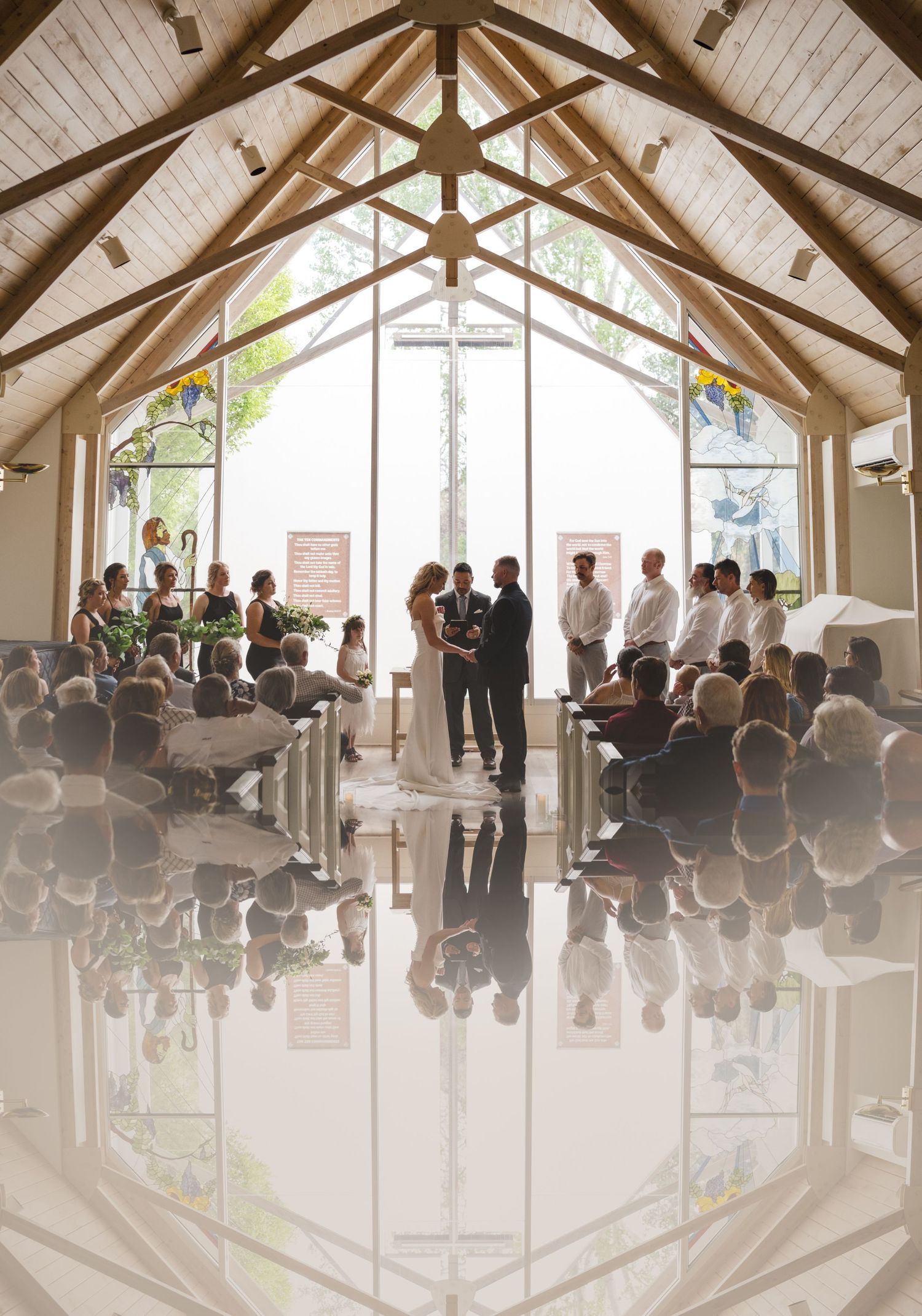 Modern chapel interior with vaulted wooden beams and gathered wedding guests reflecting on shiny floor.