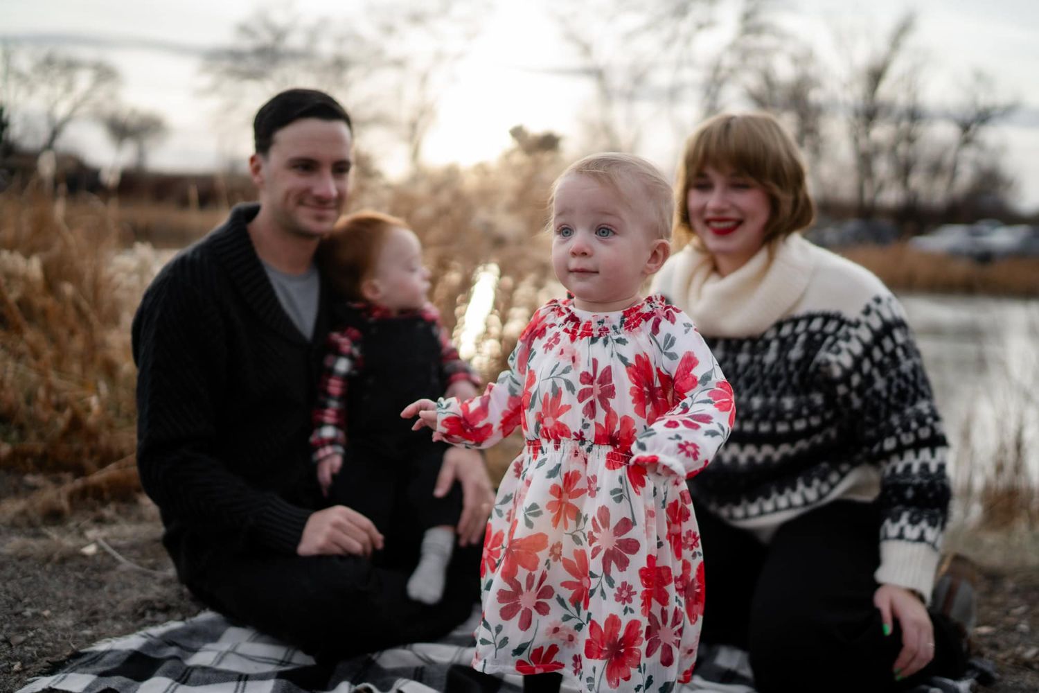A family enjoys a playful moment together outdoors by a serene lake.